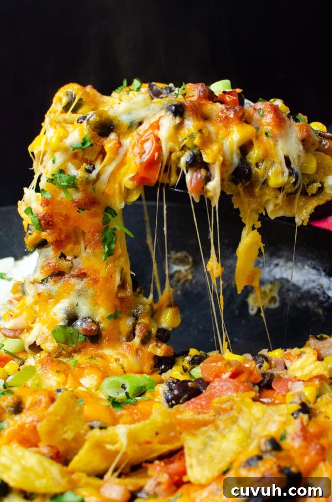 Brunch Nachos: Loaded Breakfast Nachos with Eggs & Avocado 2 Picking up nachos with a spatula and melted cheese dripping down from the nachos