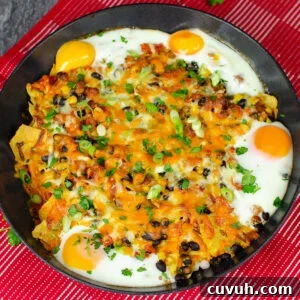 Brunch Nachos: Loaded Breakfast Nachos with Eggs & Avocado 3 Breakfast Brunch Nachos in a cast iron pan covered in melted cheese and sprinkled with chopped spring onion on red and white towel