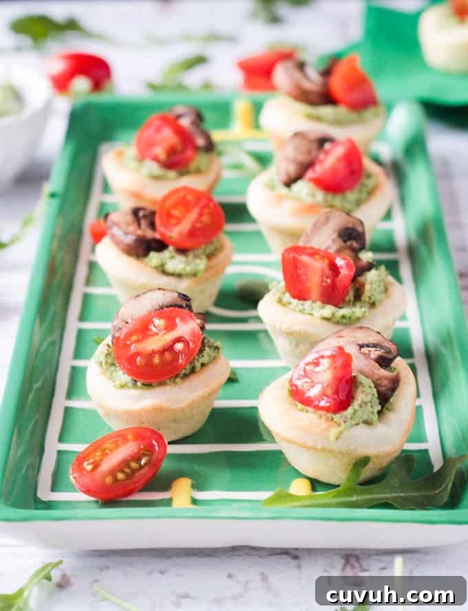 Vegan Pizza Bites - easy pizza dough topped with dairy free pesto, mushrooms and cherry tomatoes. Big bold flavors in a little bite - perfect for your next party or get together! Especially great for game day! Tray of vegan pizza bites topped with pesto, cherry tomatoes, and mushrooms.