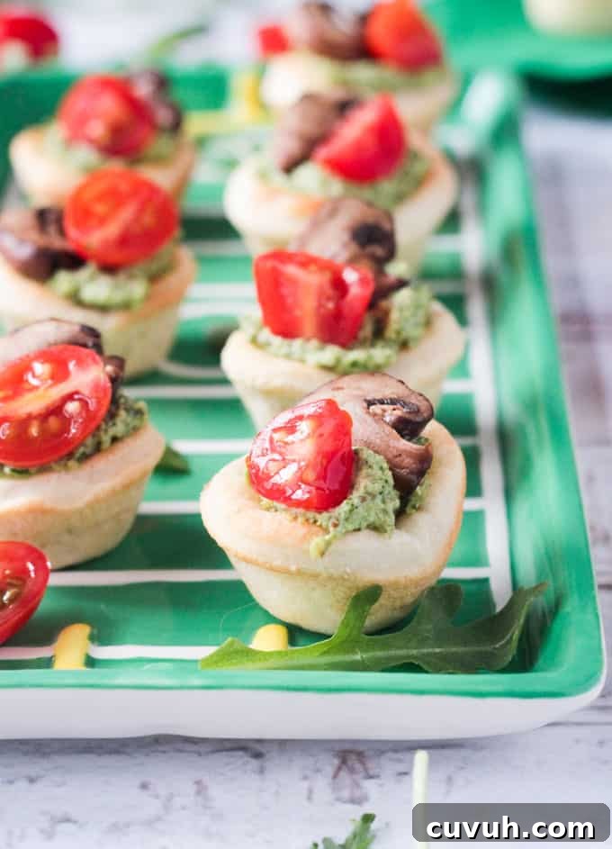 Vegan Pizza Bites - easy pizza dough topped with dairy free pesto, mushrooms and cherry tomatoes. Big bold flavors in a little bite - perfect for your next party or get together! Especially great for game day! Pizza dough formed into little bite size cups filled with pesto, tomatoes, and mushrooms.