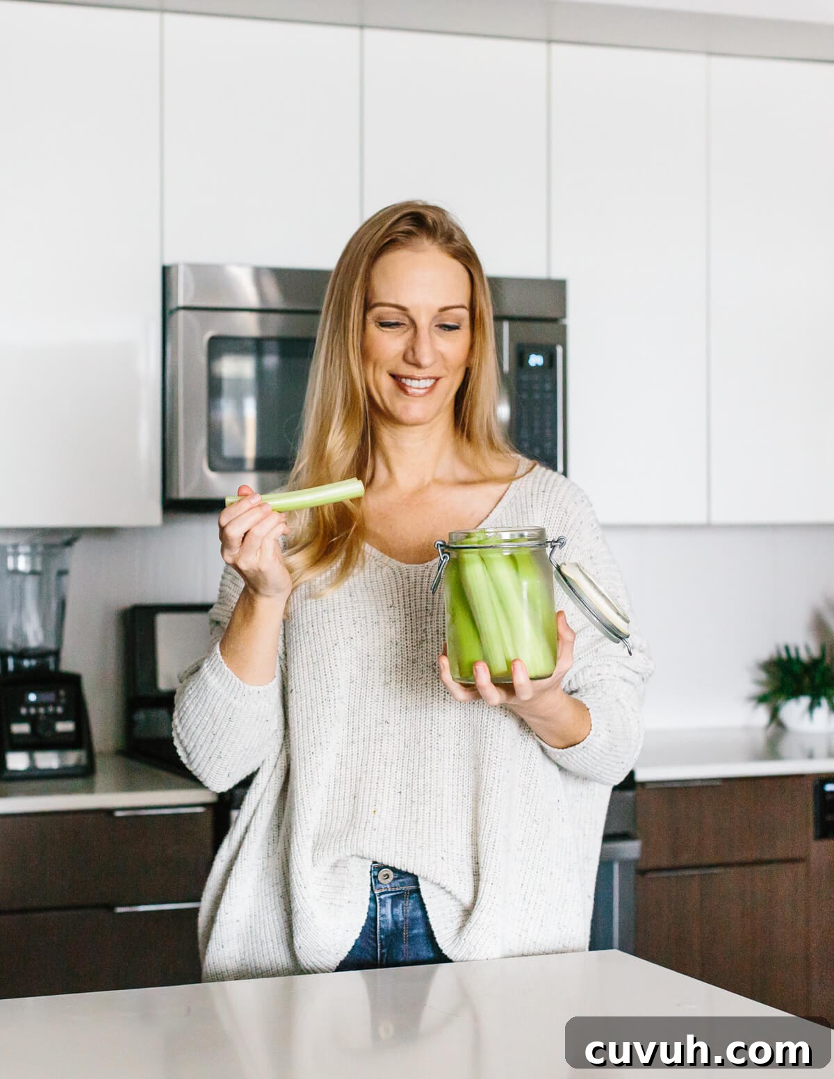 Girl standing in kitchen eating celery sticks.