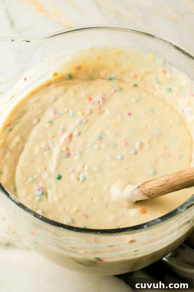 Party-Size Vanilla Birthday Sheet Cake Recipe 10 vanilla cake batter with sprinkles mixed into it, in glass mixing bowl with spatula