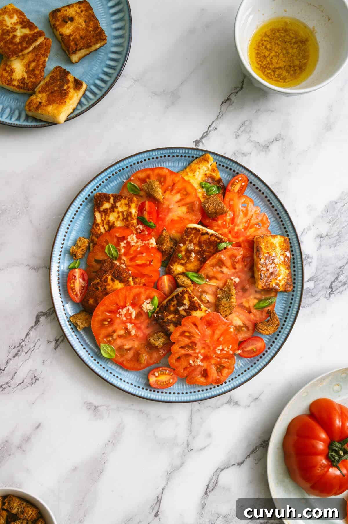 Tomato and Grilled Halloumi Salad with Basil Vinaigrette 2 Table setting with a platter of tomato and halloumi salad, fried cheese slices, and garlic dressing.