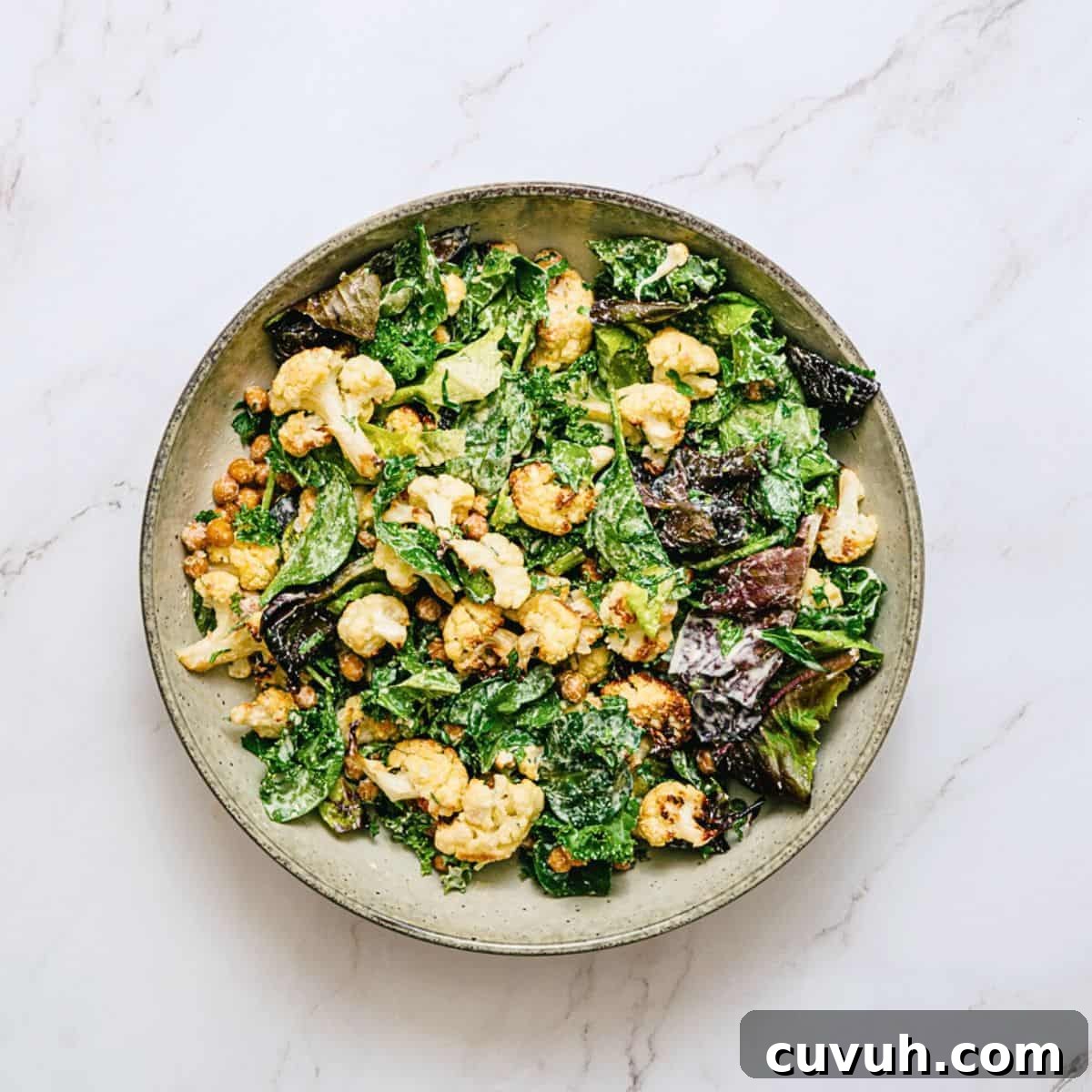 a bowl of roasted cauliflower salad on a white marble table.
