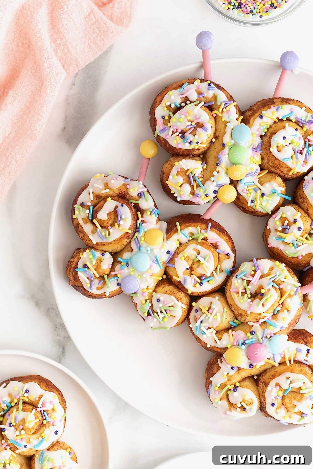 Four butterfly cinnamon rolls decorated with icing and pastel candies on a large white plate.