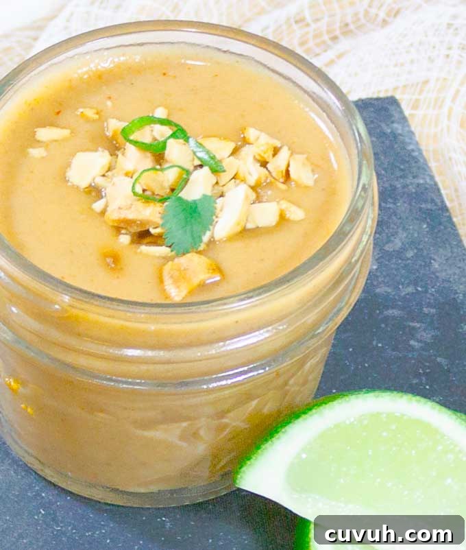 Thai Peanut Sauce Recipe in glad jar with peanut and green onion garnish
