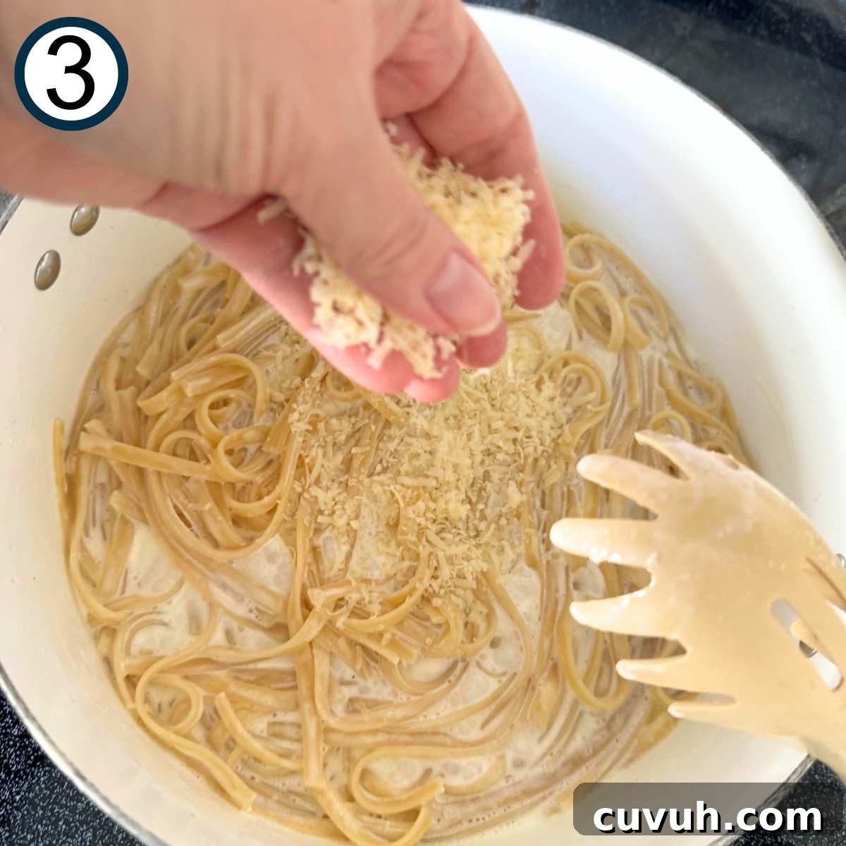 Hand dropping grated Parmesan cheese into a pot with pasta and cream.