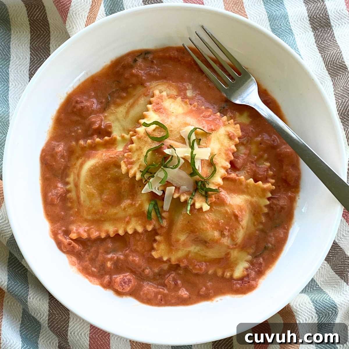 Easy lobster ravioli sauce in bowl topped with lobster ravioli, parmesan cheese, and strips of fresh basil.