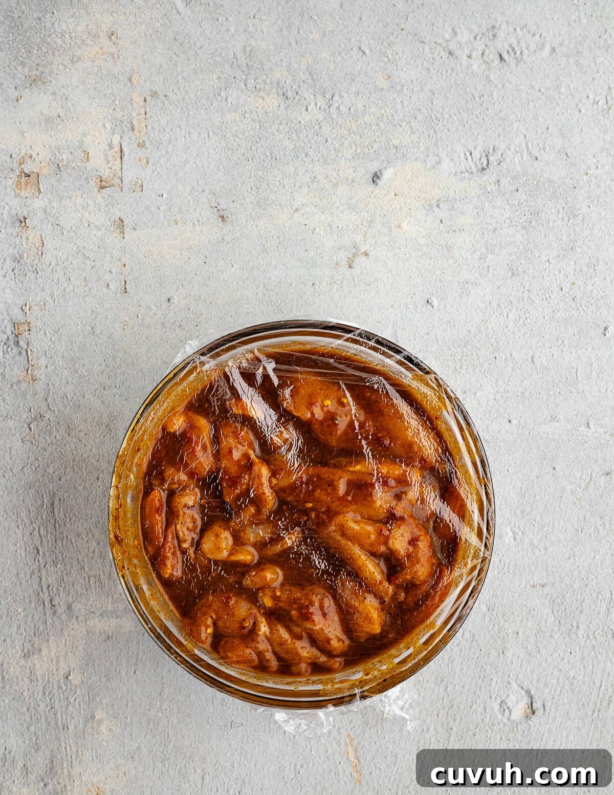 Honey Chipotle Glazed Chicken Thighs Recipe 7 a bowl of chicken thighs in a chipotle marinade with saran wrap on top.