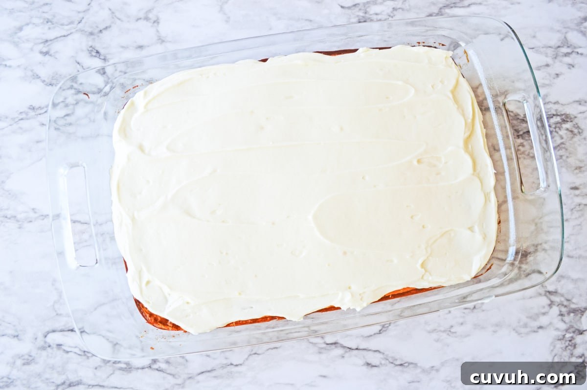 frosting layer spread on top of baked cake in glass pan