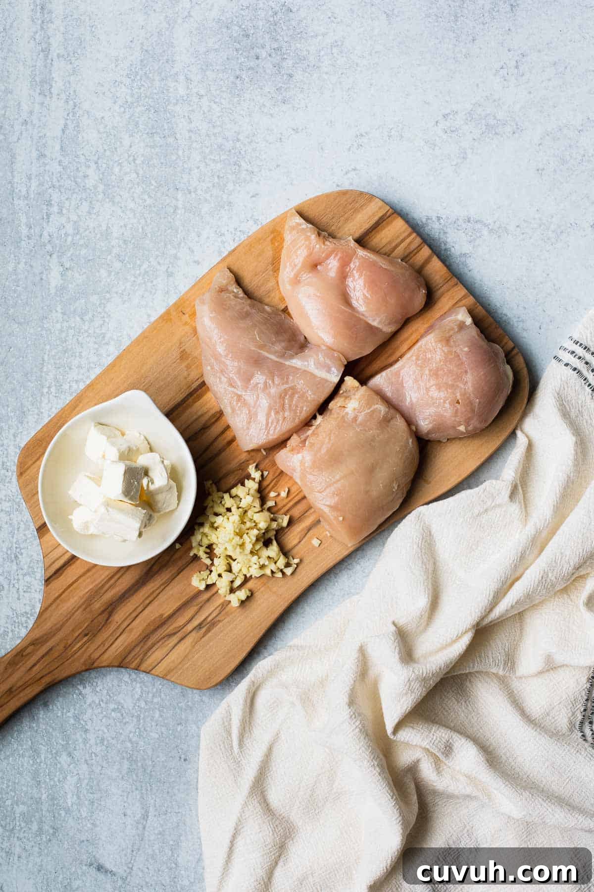 Creamy Instant Pot Chicken Alfredo Recipe in 30 Minutes 4 cut chicken, minced garlic, cubed cream cheese on a cutting board