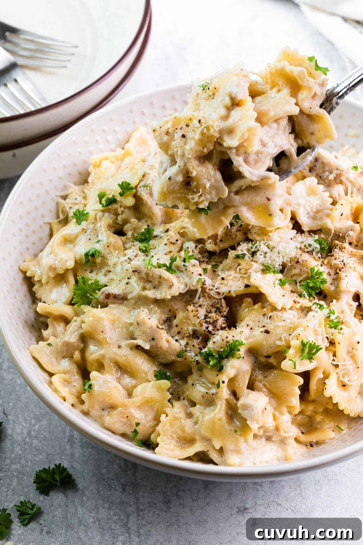 Creamy Instant Pot Chicken Alfredo Recipe in 30 Minutes 9 close up view of a fork taking a bite out of a white bowl filled with pasta in a creamy white sauce