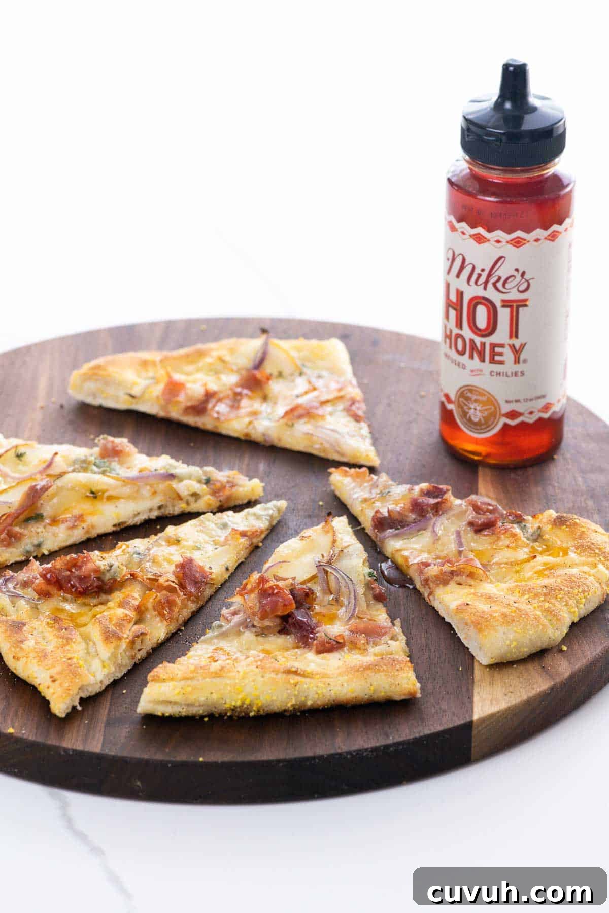 pear gorgonzola pizza with prosciutto and hot honey on a cutting board with a bottle of hot honey