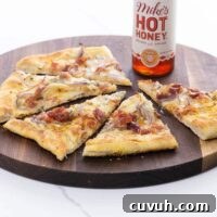 pear gorgonzola pizza with prosciutto and hot honey on a cutting board with a bottle of hot honey