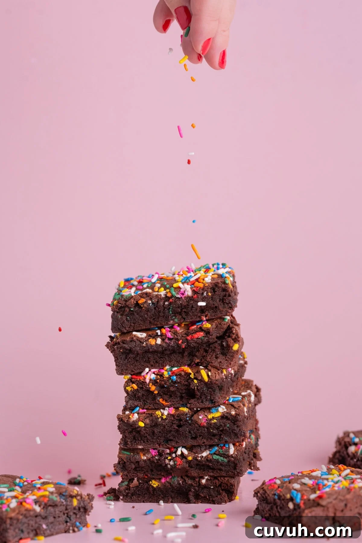Dropping rainbow sprinkles onto a stack of Funfetti brownies.