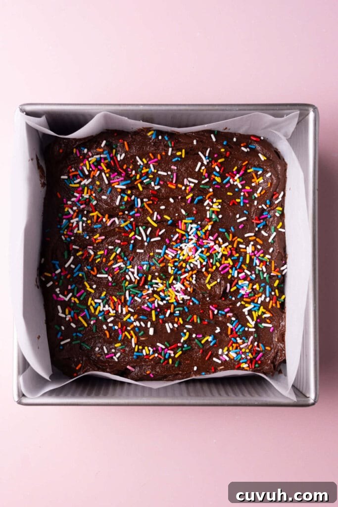 Fudgy brownie batter in a lined pan topped with rainbow sprinkles.