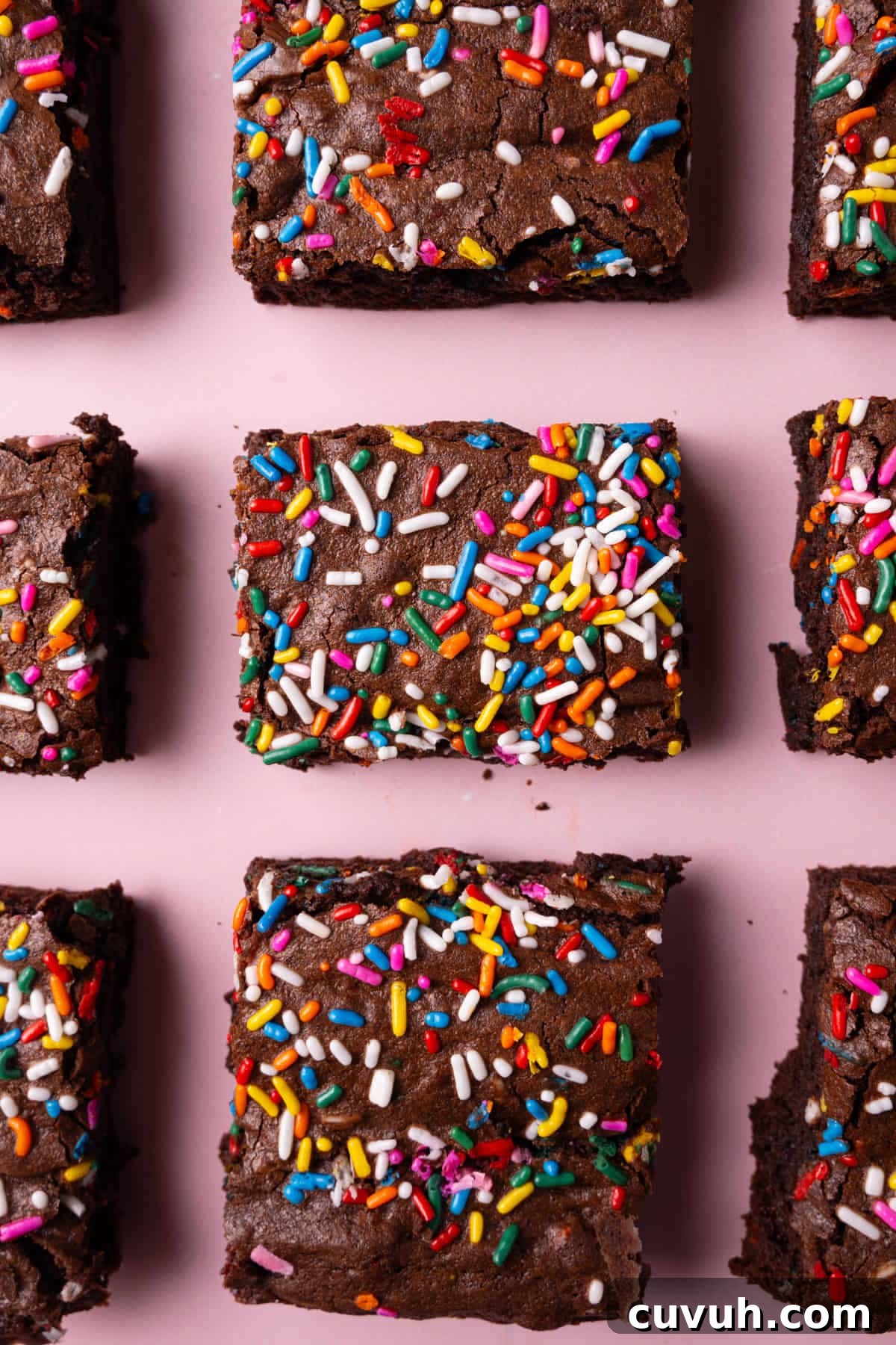 Overhead image of sliced brownies with rainbow sprinkles on a pink background.