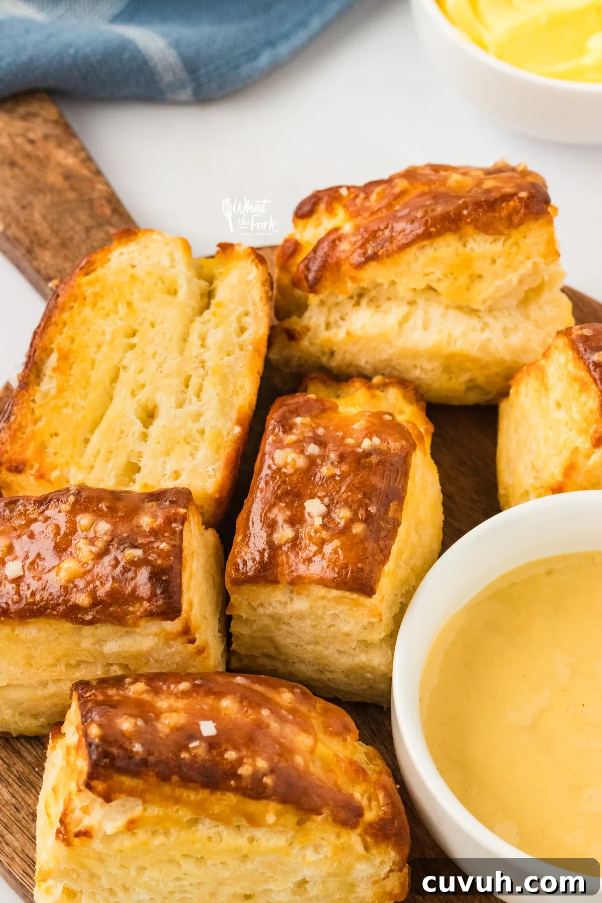 Buttery Prezel Biscuits on a round wood serving platter with a handle with a small white bowl of honey mustard