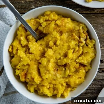 Cooked corn casserole in white bowl with spoon inserted into the casserole.