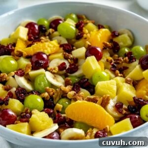 Fruit salad mixed with honey lime dressing in a white bowl.