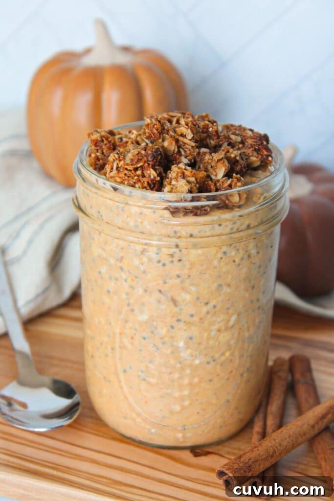 Pumpkin Protein Overnight Oats Recipe for Morning Energy 6 A mason jar full of pumpkin flavored overnight oats topped with granola and on a wooden board with pumpkins in the background and a spoon on the side.