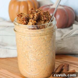A mason jar full of pumpkin flavored overnight oats topped with granola and on a wooden board with pumpkins in the background.