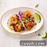 Chili lime shrimp tacos on a small white plate with a lime wedge to the side.