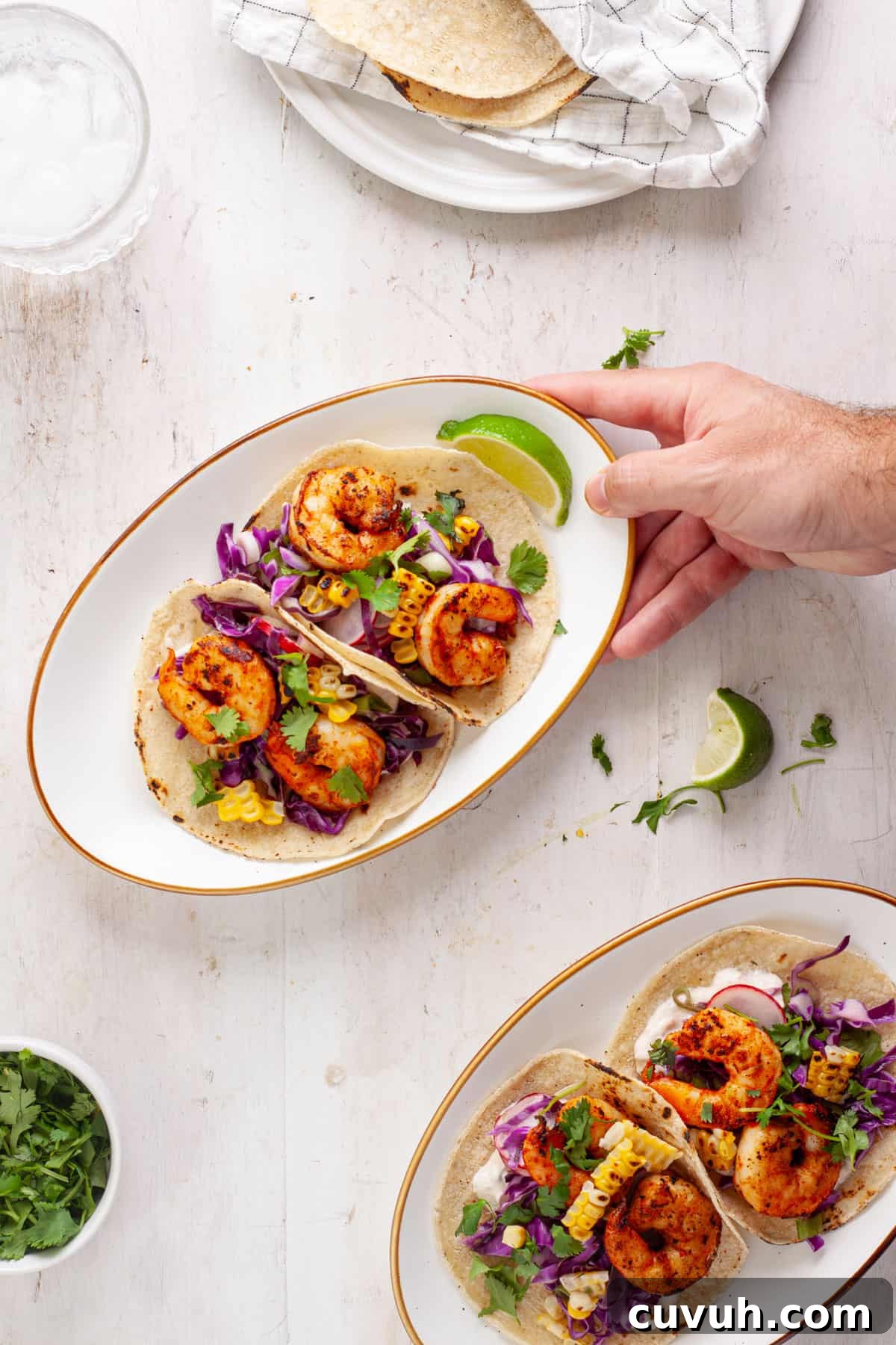 A hand placing a plate of chili lime shrimp tacos.
