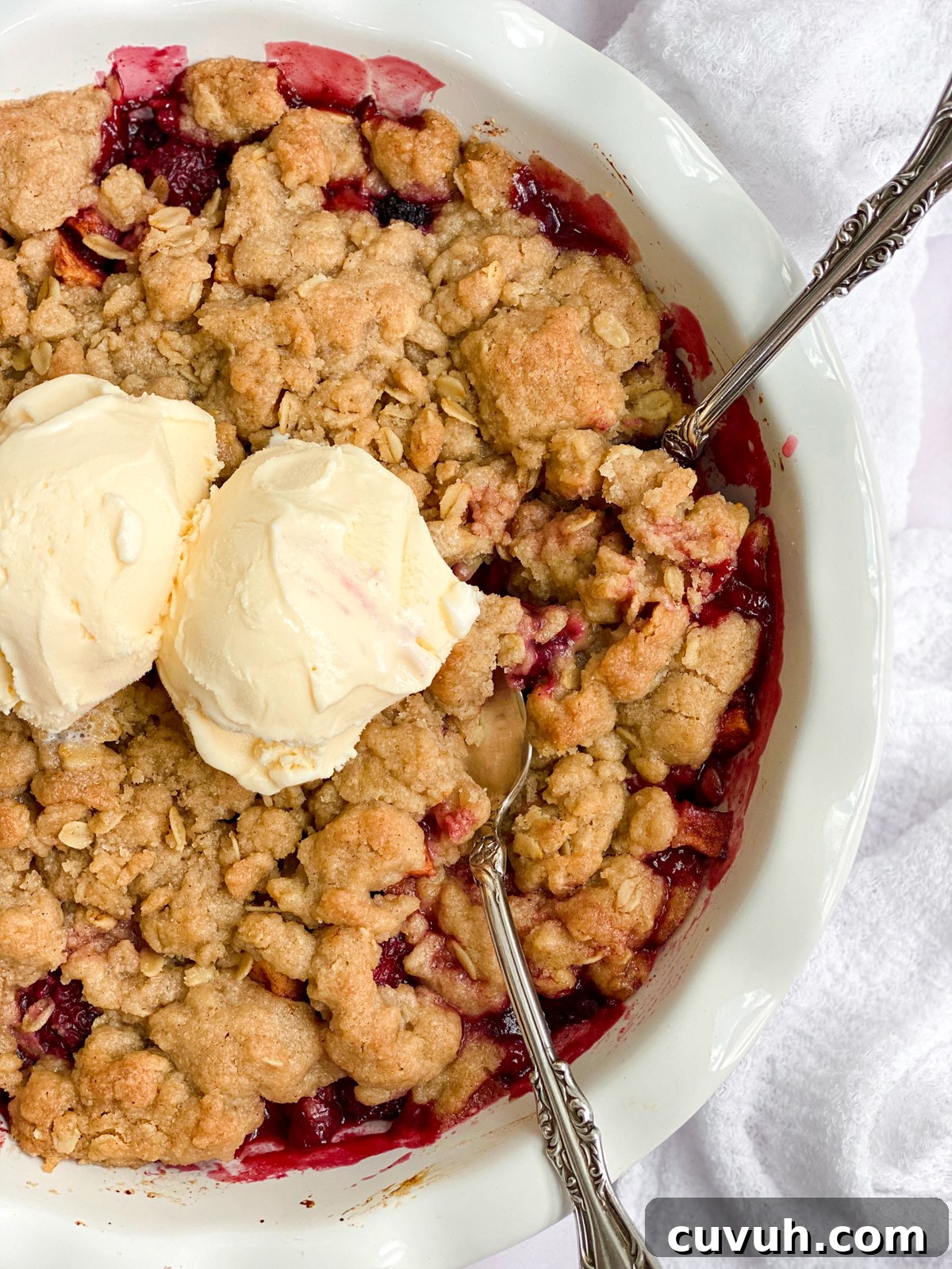 Blackberry Apple Crumble Recipe with Crisp Golden Topping 3 close up of the blackberry and apple crumble with 2 scoops of ice cream and 2 spoons in.