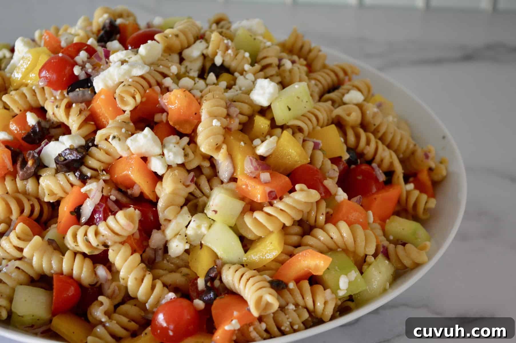 Whole Wheat Greek Pasta Salad with Feta & Olives 2 Whole Wheat Greek Pasta Salad with feta, tomatoes, cucumbers, and bell pepper in an white bowl.