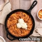 A cast iron skillet of stone fruit cobbler topped with scoops of vanilla ice cream.