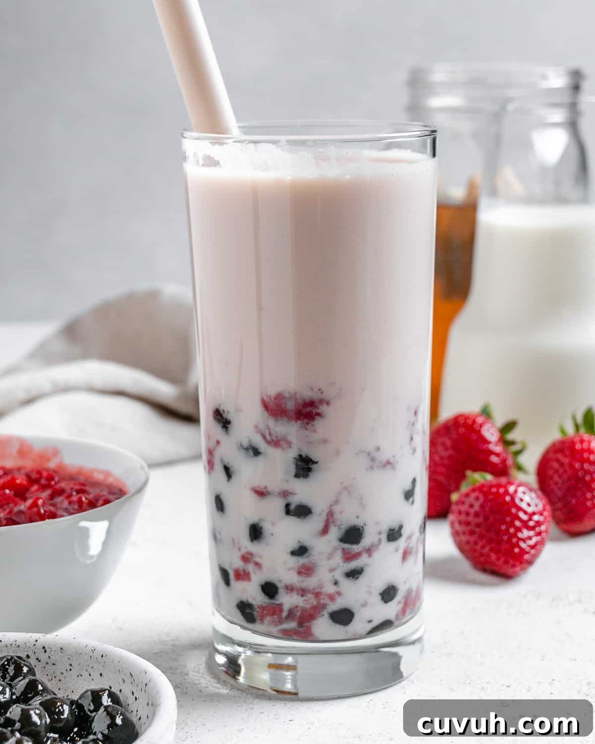 completed Strawberry Boba Tea in a glass cup with ingredients in the background