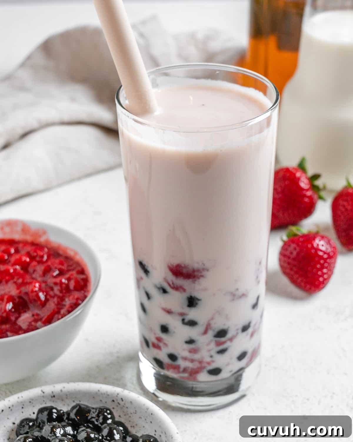 completed Strawberry Boba Tea in a glass cup with ingredients in the background