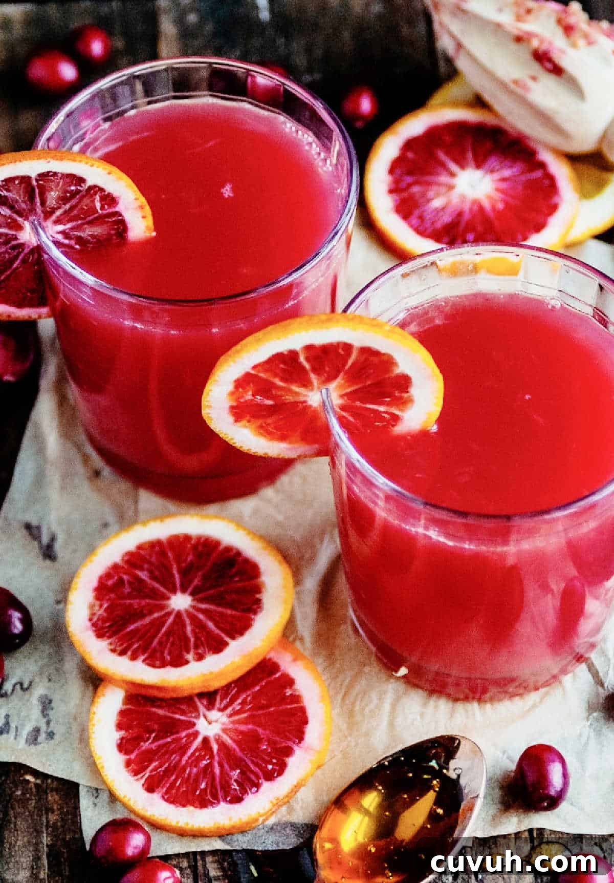 Madras Cocktail Recipe: How to Make the Classic Cranberry Vodka Drink 2 Orange slices and cranberries around two glasses with cranberry orange cocktail on a white and wood surface.