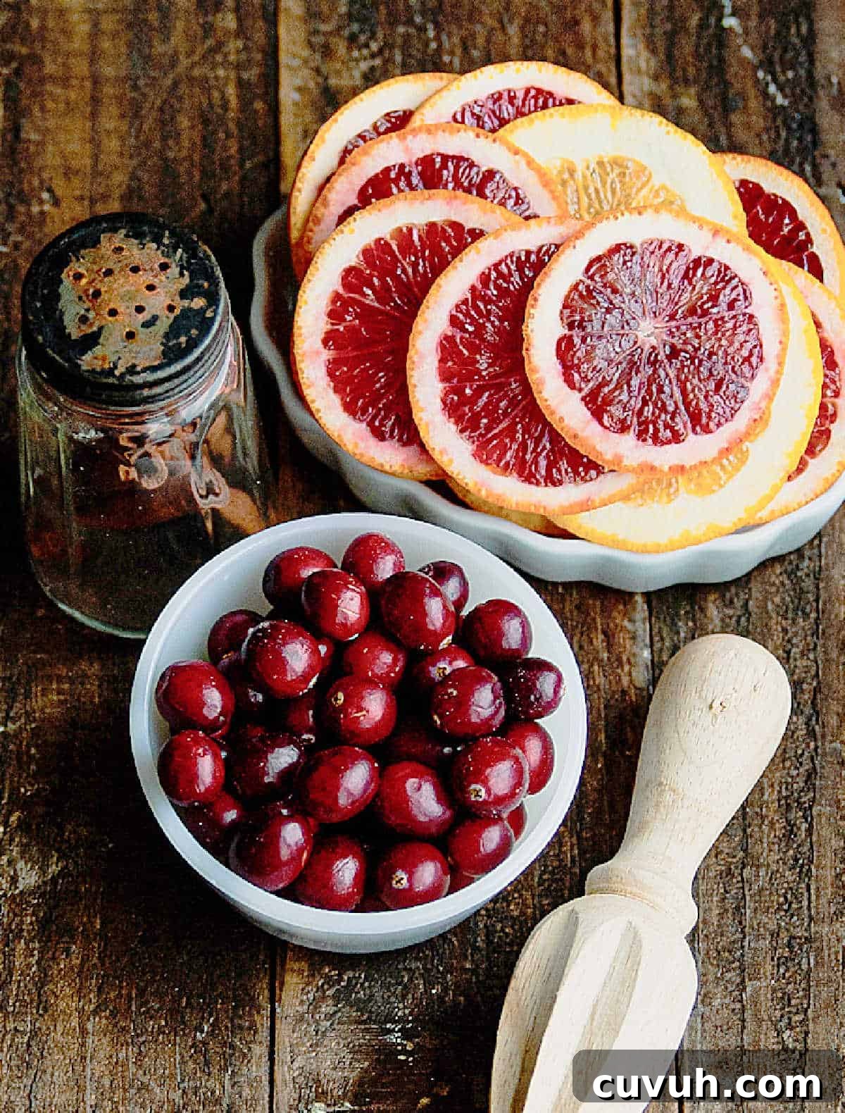 Madras Cocktail Recipe: How to Make the Classic Cranberry Vodka Drink 3 Bowls with cranberries and blood orange slices on a wooden surface. Citrus wooden hand juicer.