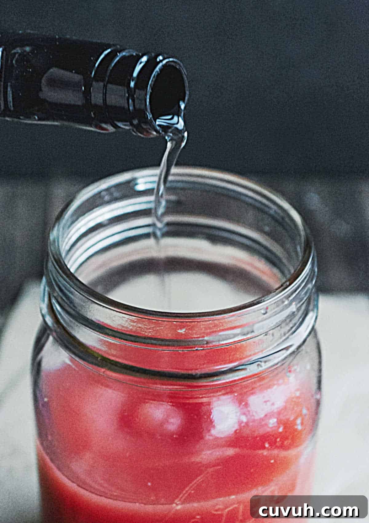Madras Cocktail Recipe: How to Make the Classic Cranberry Vodka Drink 4 Glass mason jar with cranberry juice. Vodka being poured into it. White surface and black background.