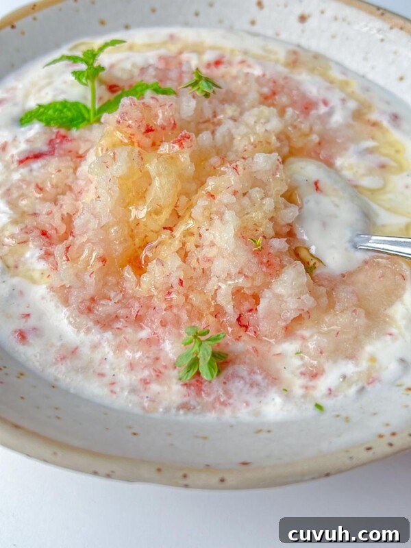 A bowl of yogurt topped with crushed ice, honey, and fresh mint leaves.