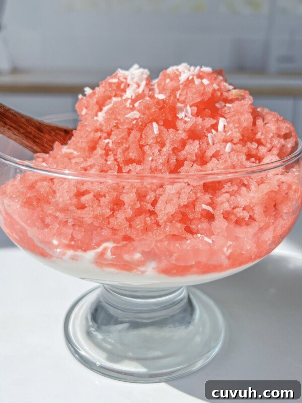 A glass dessert bowl filled with bright pink shaved ice topped with shredded coconut.