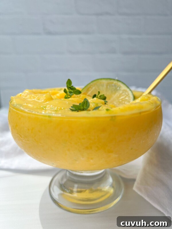 A glass dessert bowl filled with creamy yellow mango frozen yogurt, garnished with a lime slice.