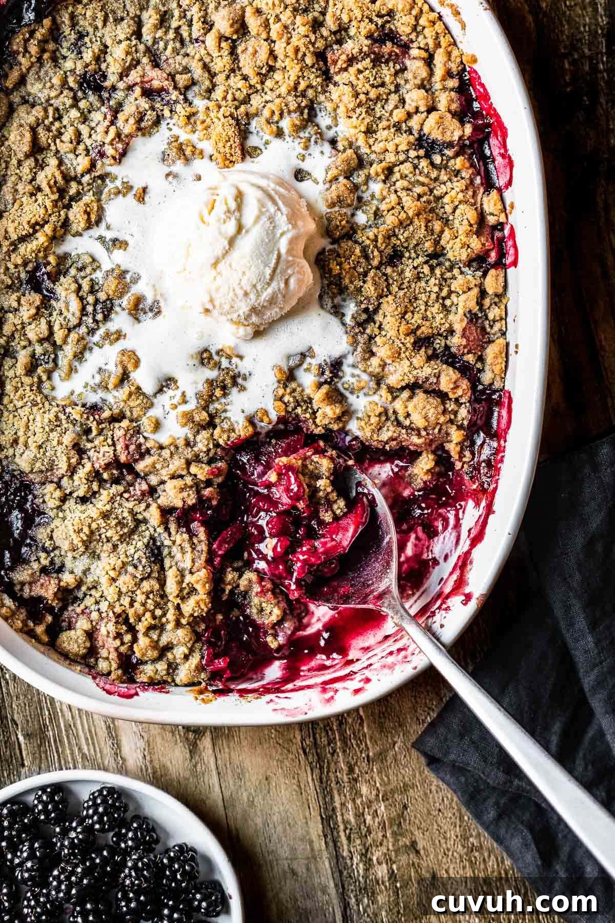 Apple and Blackberry Crumble Recipe for Perfect Autumn Dessert 2 Fruit crumble in a ceramic dish with a scoop of vanilla ice cream on top.