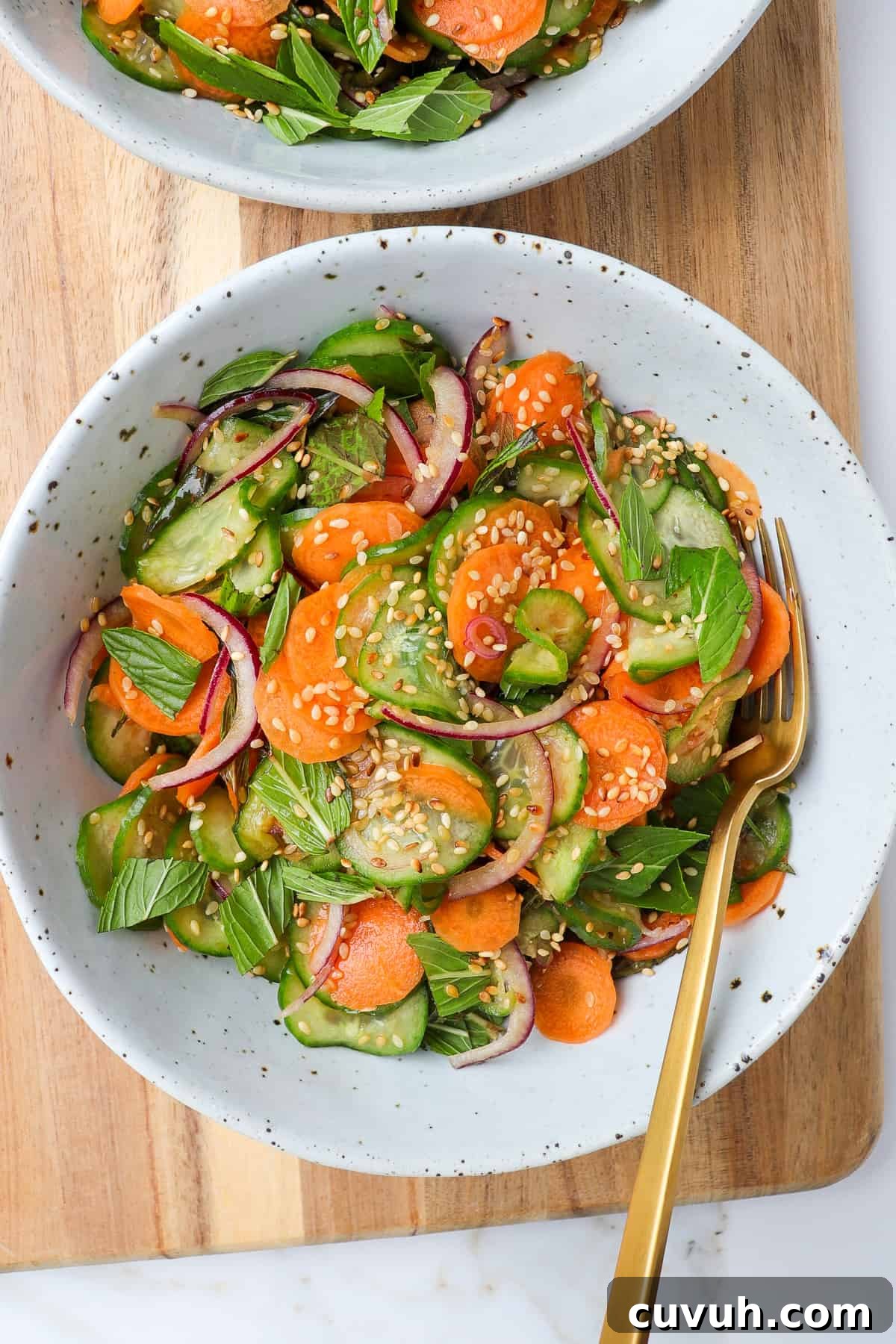 Sesame Carrot and Cucumber Salad with Tangy Dressing 2 Carrot cucumber salad in bowls with fork on a wooden board.