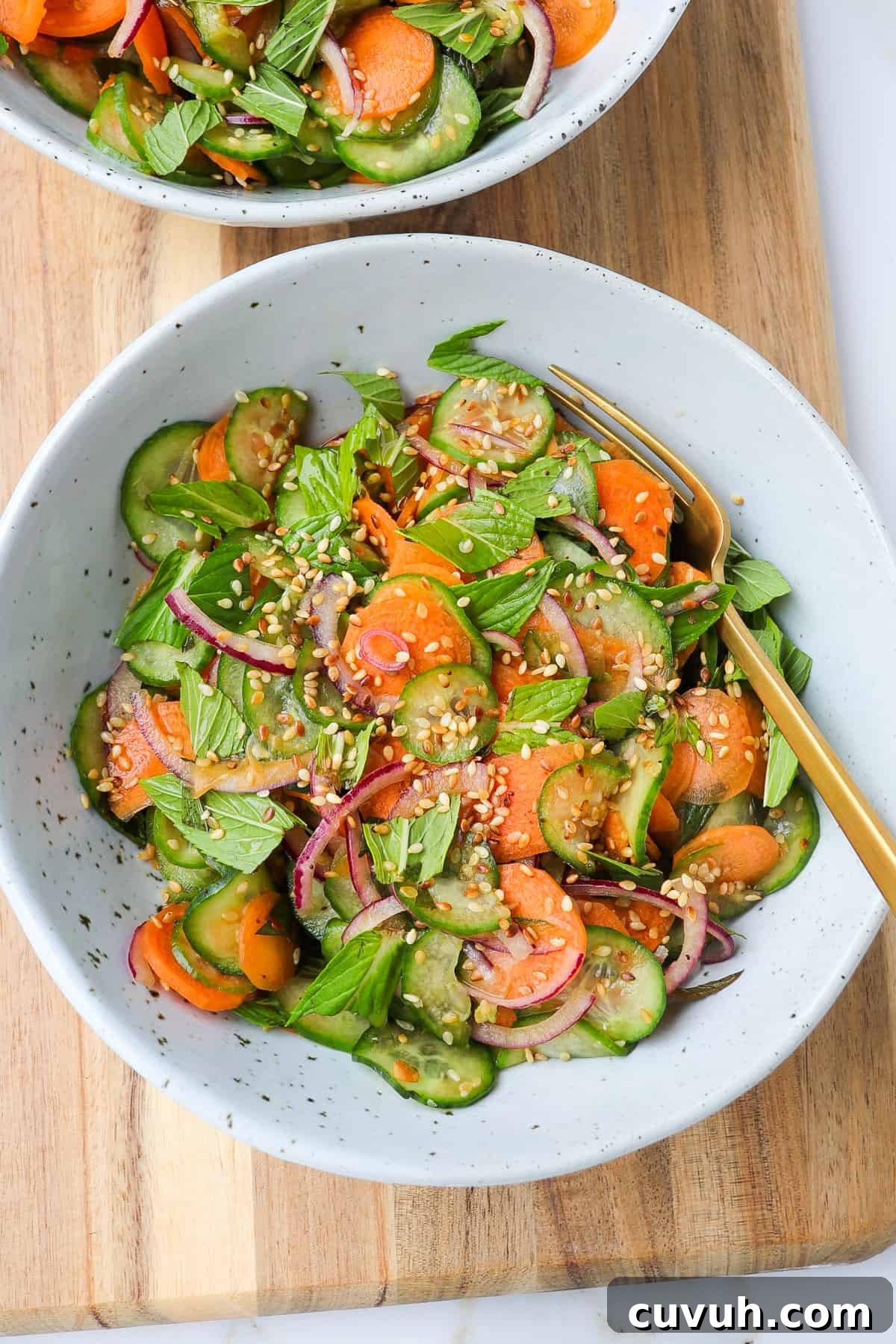 Sesame Carrot and Cucumber Salad with Tangy Dressing 9 Carrot cucumber salad in bowls with fork on a wooden board.