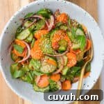 Carrot cucumber salad in bowls with fork on a wooden board.
