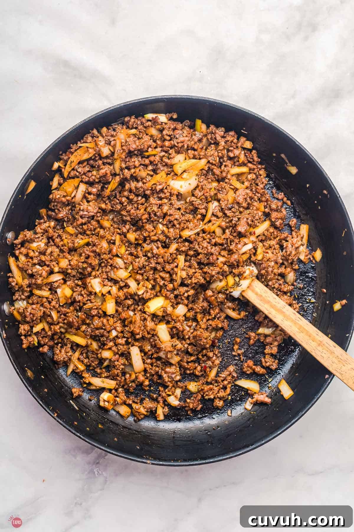 cooked ground beef in a skillet with a wood spoon