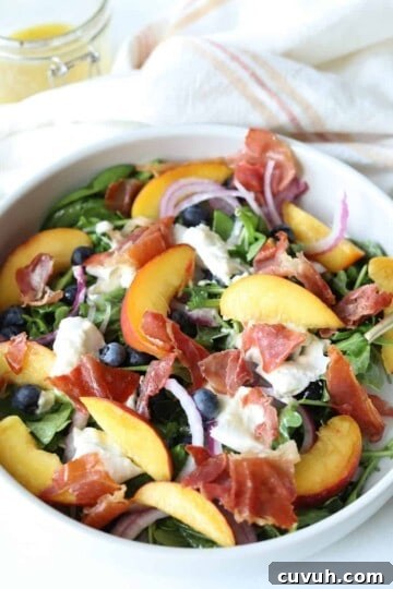 peach burrata salad in large white bowl with gold fork