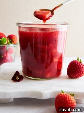 A spoon lifting a scoop of strawberry sauce from a jar.