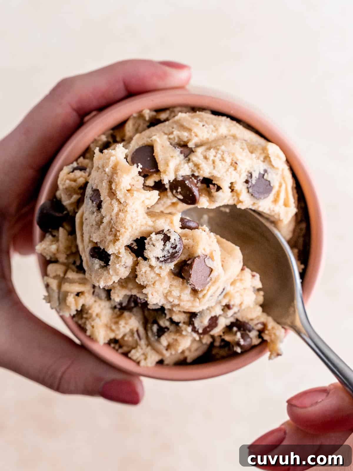 Top view of a scoop of edible chocolate chip cookie dough in a cup with a spoon digging into it.