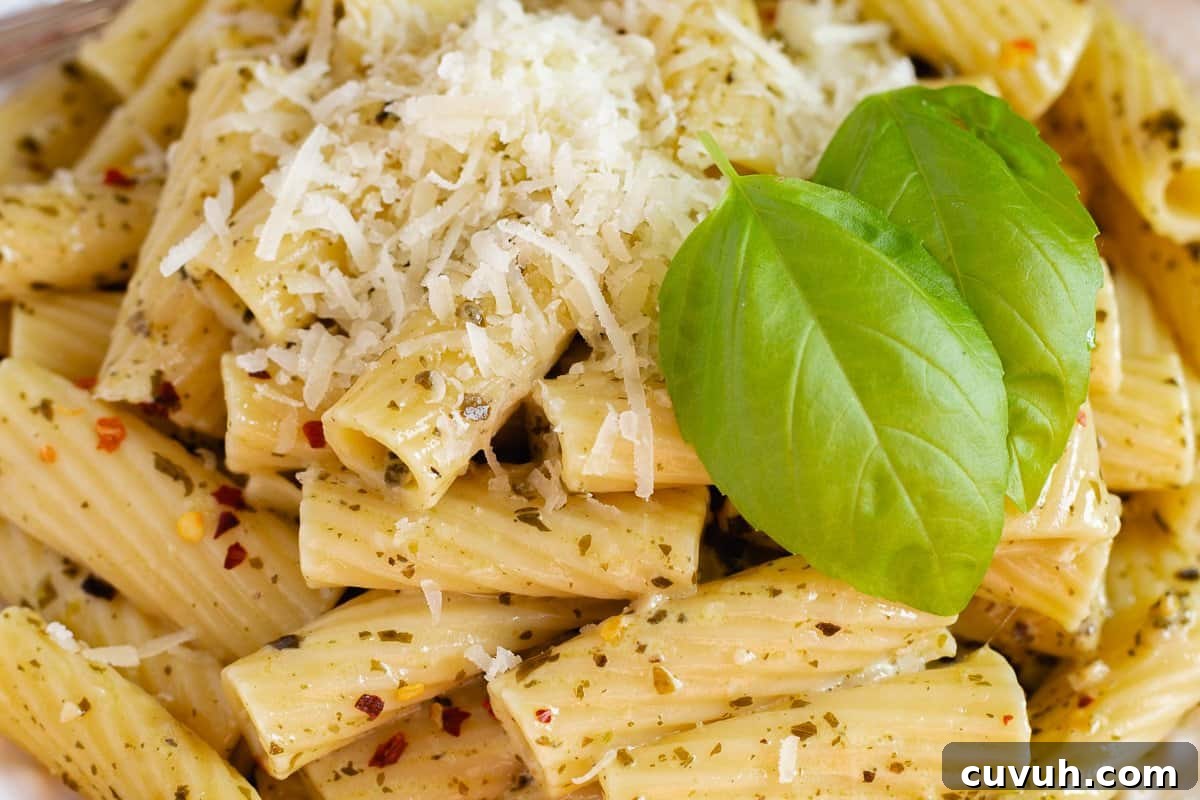 Pesto pasta served on a plate with grated parmesan cheese.