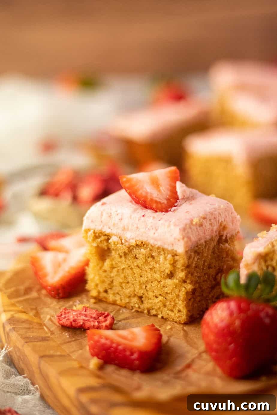 Peanut Butter Layer Cake with Strawberry Buttercream Frosting 11 side angle shot of sliced peanut butter cake with strawberry frosting on a wooden cutting board. sliced strawberries scattered in perimeter of shot.
