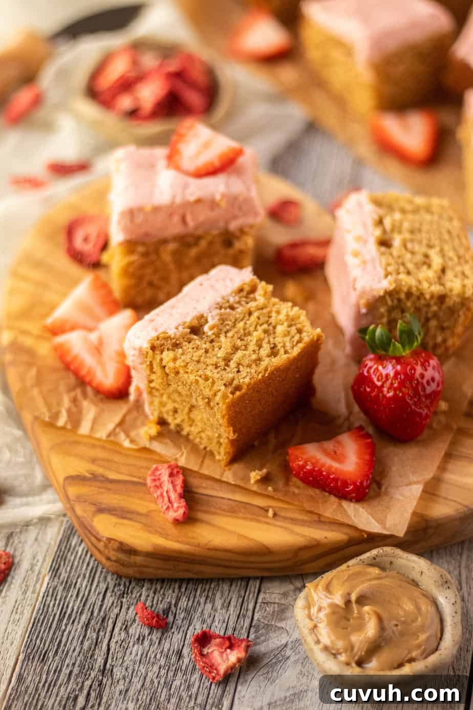 Peanut Butter Layer Cake with Strawberry Buttercream Frosting 12 side angle shot of sliced peanut butter cake with strawberry frosting on a wooden cutting board. sliced strawberries scattered in perimeter of shot.